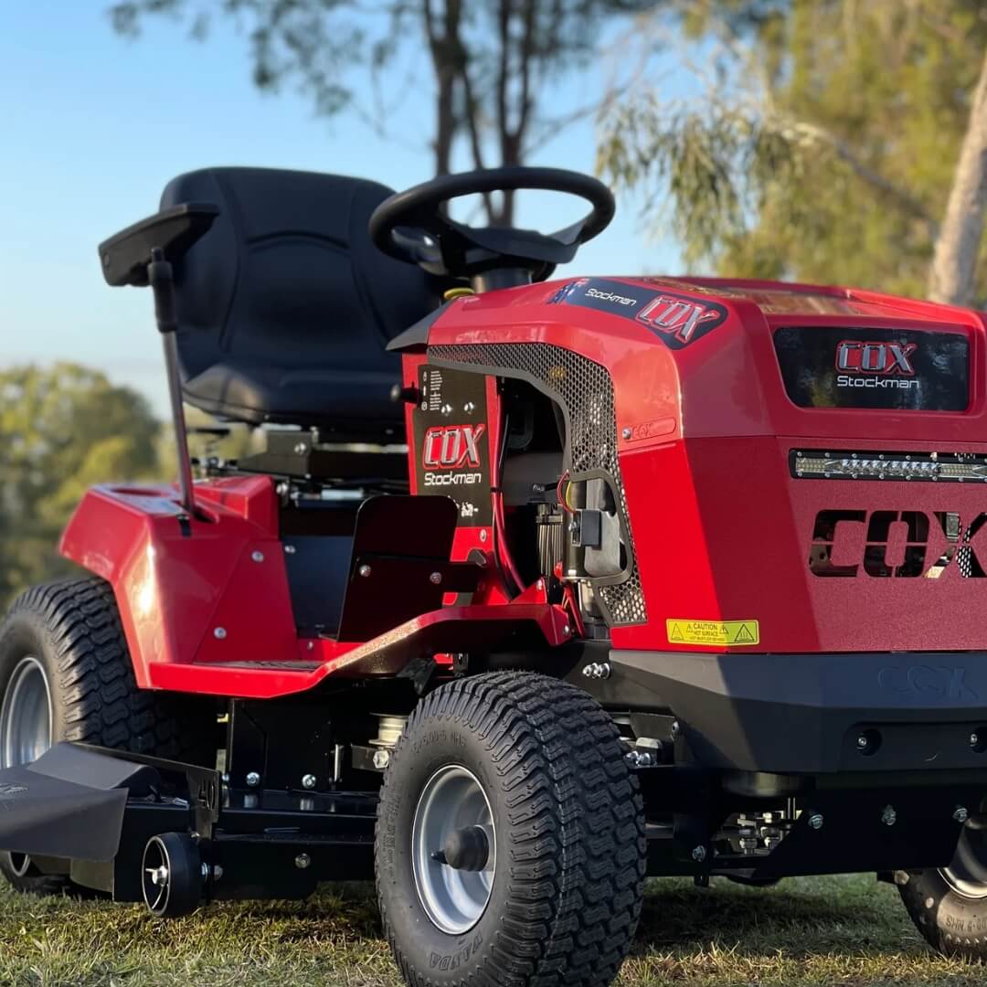 Red lawn tractor with 'COX' branding on a grassy field.