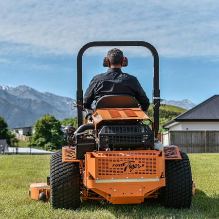 Person operating a large orange lawn mower with mountains in the background