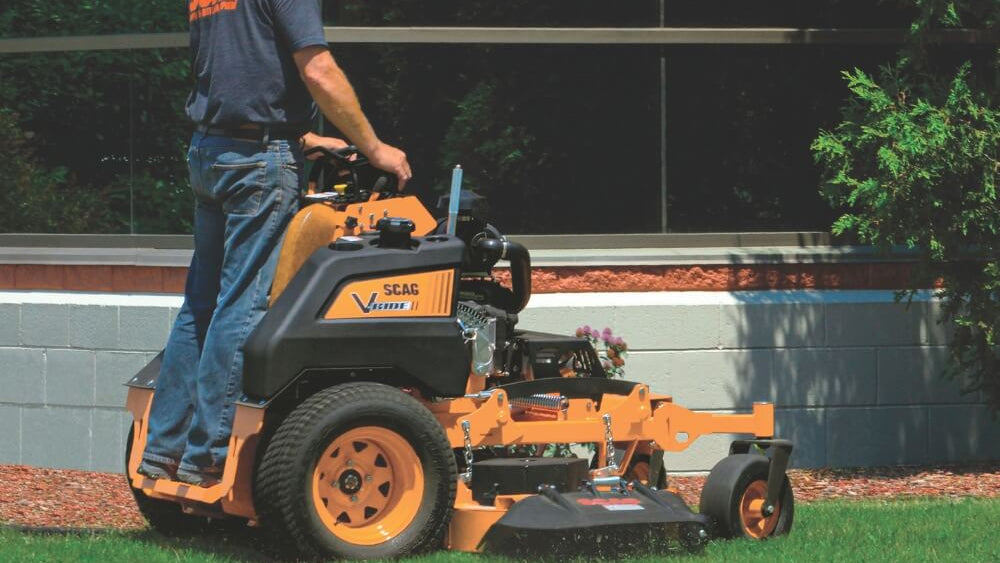 Man operating a riding lawn mower on grass with a building in the background